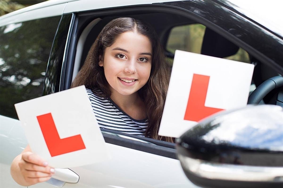 A smiling learner driver holding L plates at the car window