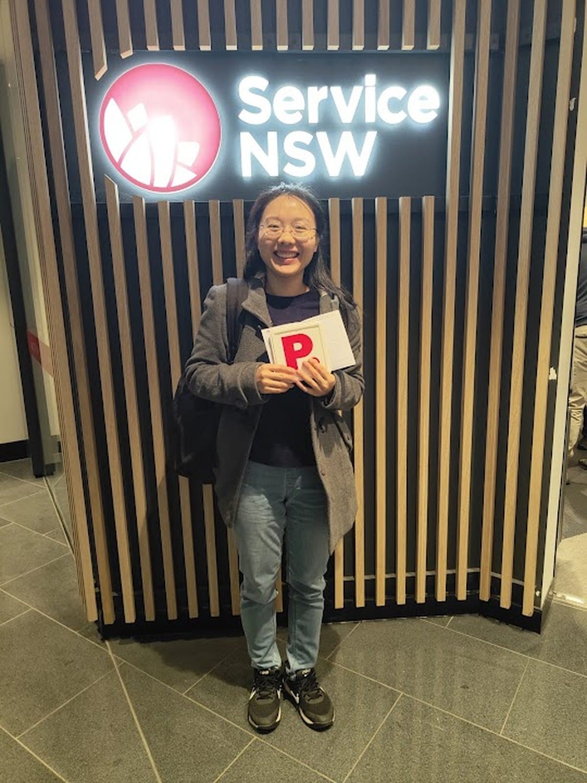 A new driver smiling and holding P plates inside a Service NSW centre