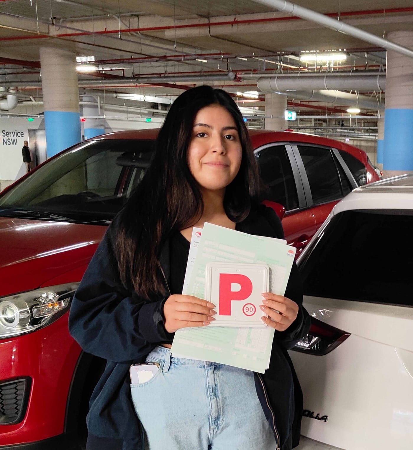 A new driver holding P plates and paperwork in a car park