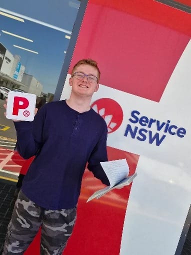 A smiling new driver holding P plates outside a Service NSW centre
