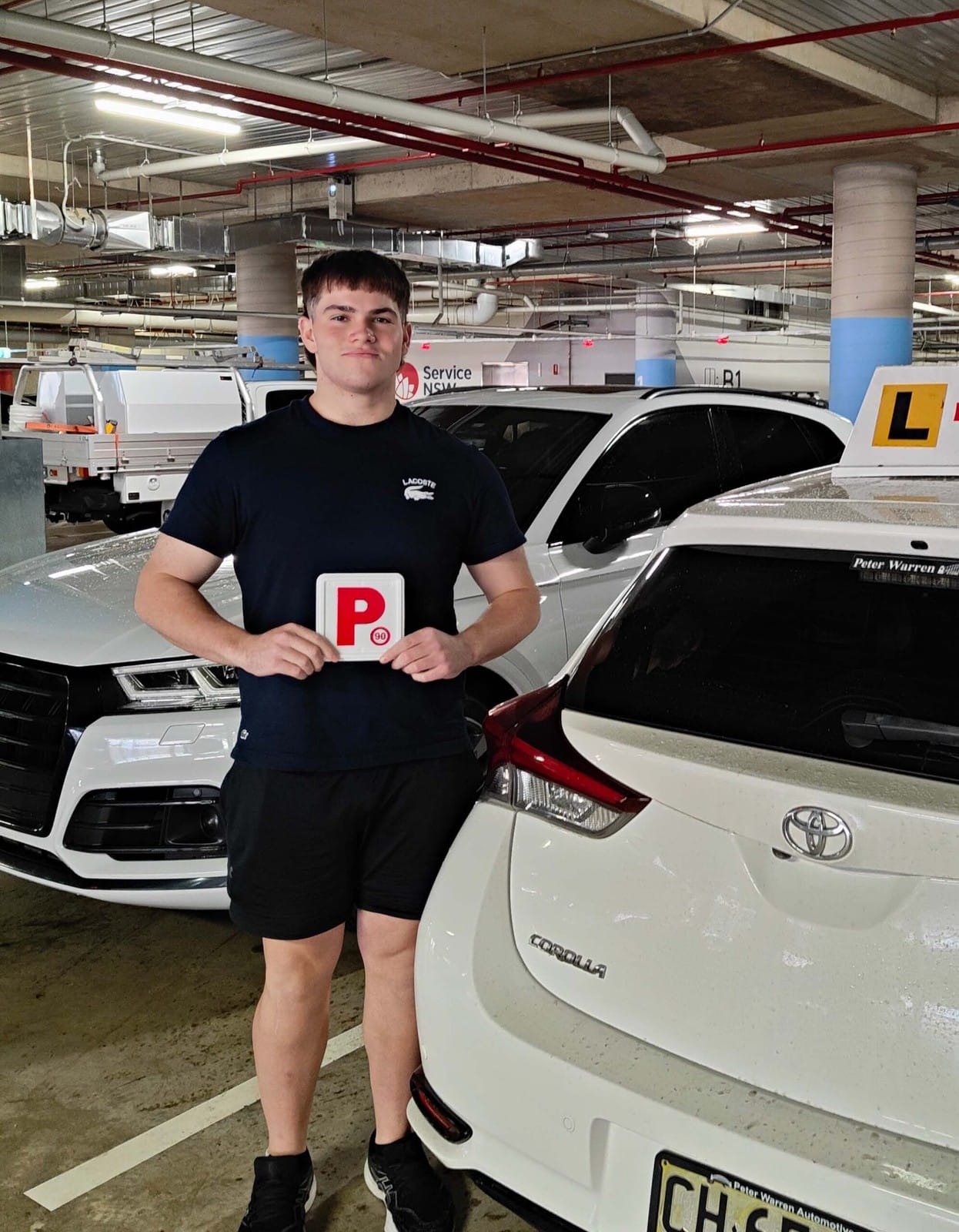 A new driver holding P plates beside a training car